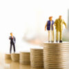 Old couple walking on pile of coins, businessman behind them on other pile of coins